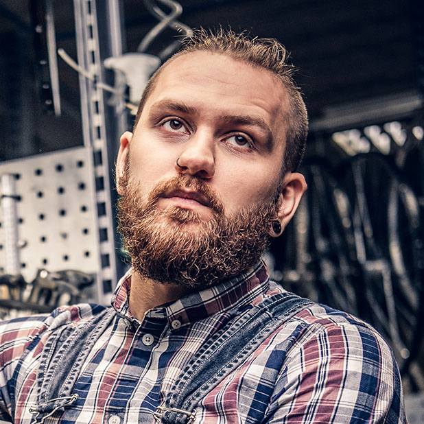 Bearded mechanic doing bicycle wheel service manual in a workshop.