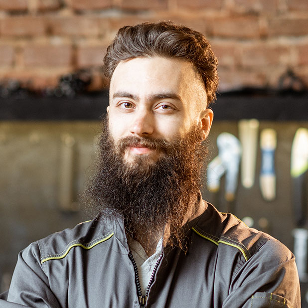 Portrait of a handsome bearded repairman in workwear standing with wrenches at the bicycle workshop